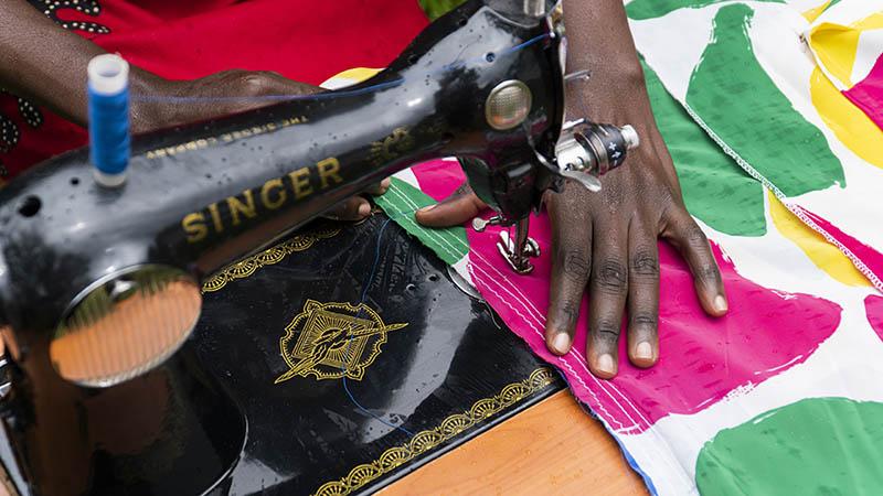 Ugandalainen nainen ompelee Singerin ompelukoneella värikästä kangasta